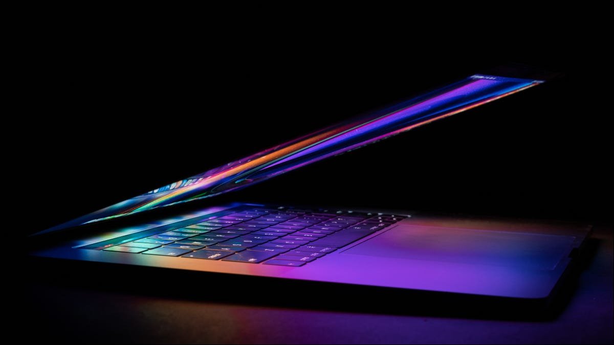 MacBook semicerrado con colores brillantes de la pantalla reflejados en el teclado.